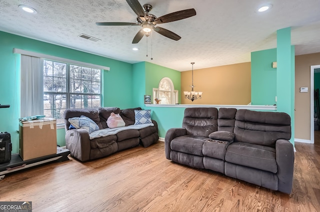 living room with ceiling fan with notable chandelier, a textured ceiling, and light hardwood / wood-style flooring