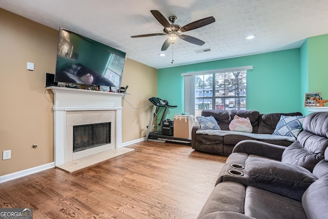 living room with a fireplace, a textured ceiling, light hardwood / wood-style floors, and ceiling fan