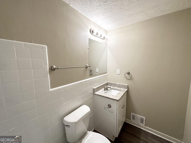 bathroom featuring vanity, a textured ceiling, wood-type flooring, tile walls, and toilet