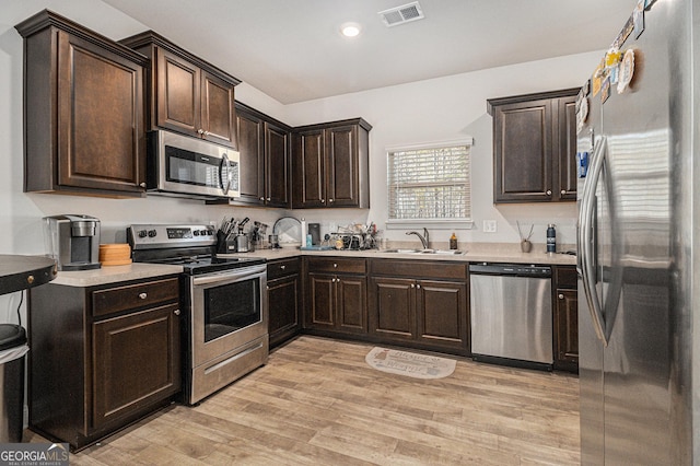 kitchen featuring dark brown cabinets, light wood-type flooring, stainless steel appliances, and sink