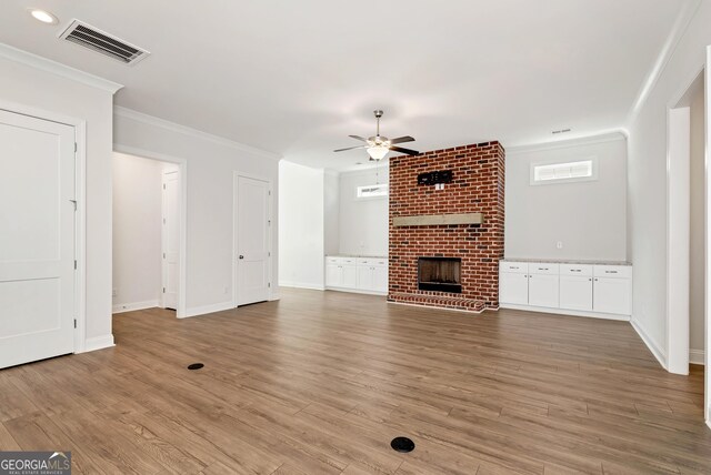 unfurnished living room featuring light wood-type flooring, a brick fireplace, ceiling fan, and ornamental molding