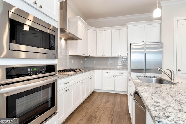 kitchen featuring tasteful backsplash, wall chimney exhaust hood, stainless steel appliances, sink, and hanging light fixtures