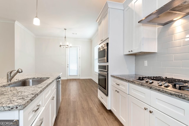 kitchen featuring appliances with stainless steel finishes, sink, wall chimney range hood, pendant lighting, and white cabinets