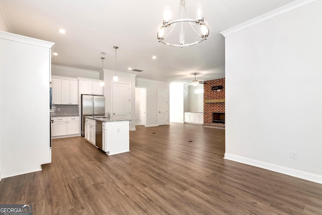 kitchen featuring white cabinetry, a brick fireplace, stainless steel dishwasher, decorative light fixtures, and a kitchen island with sink