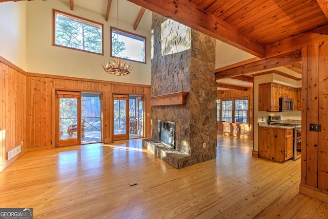 living room featuring beam ceiling, french doors, a stone fireplace, light hardwood / wood-style flooring, and a towering ceiling