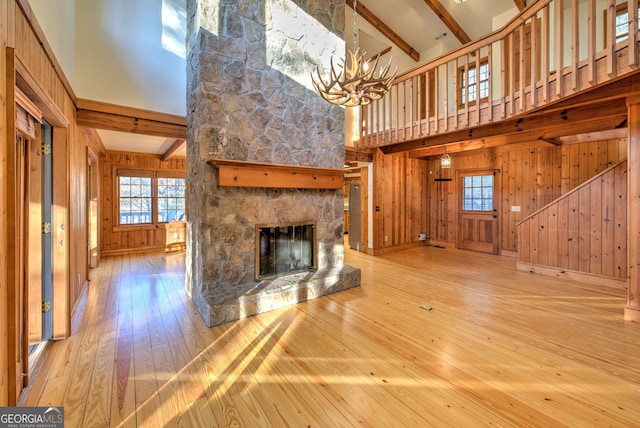 unfurnished living room featuring light wood-type flooring, a fireplace, high vaulted ceiling, beamed ceiling, and wood walls