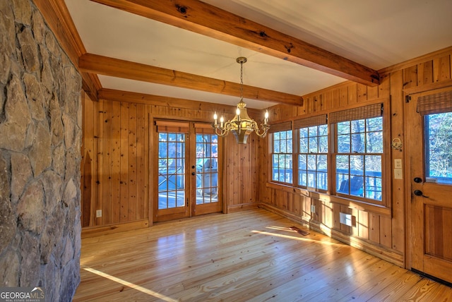 unfurnished dining area featuring beamed ceiling, wooden walls, light hardwood / wood-style floors, and a notable chandelier