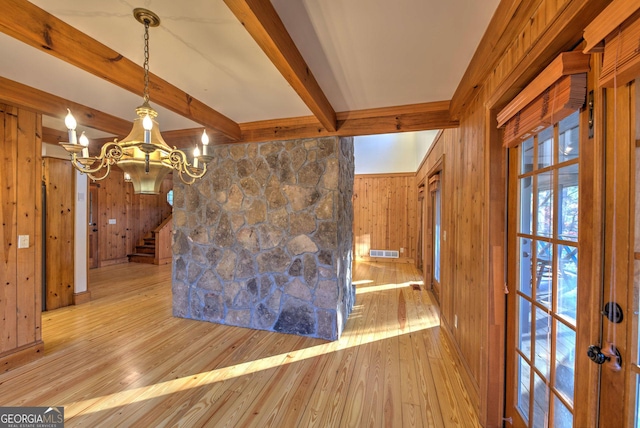 unfurnished dining area featuring wood walls, a notable chandelier, beam ceiling, and light wood-type flooring