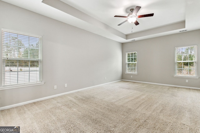 carpeted empty room with a raised ceiling and ceiling fan