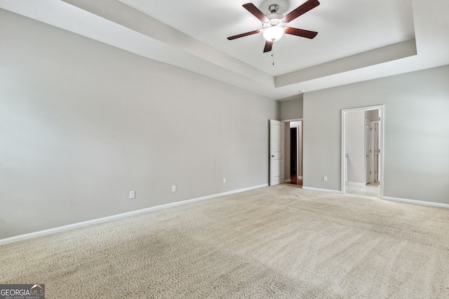 empty room with light colored carpet, a raised ceiling, and ceiling fan