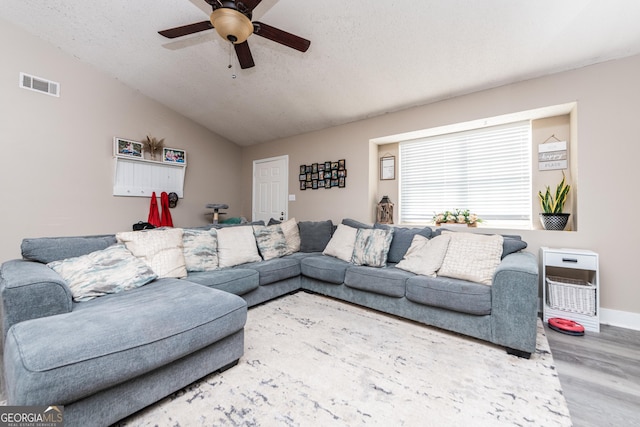 living area featuring visible vents, a ceiling fan, vaulted ceiling, a textured ceiling, and wood finished floors