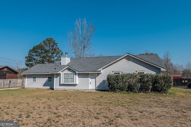 back of property with a shingled roof, a lawn, a chimney, and fence