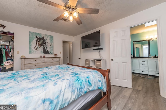 bedroom featuring visible vents, a ceiling fan, wood finished floors, a textured ceiling, and a sink