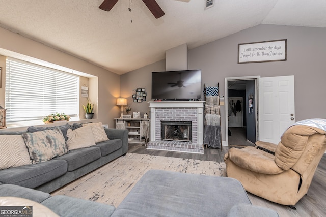 living room with a brick fireplace, a ceiling fan, vaulted ceiling, and wood finished floors