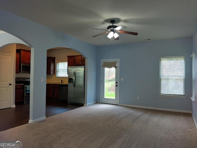 unfurnished living room with ceiling fan and dark colored carpet