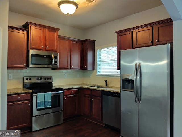 kitchen with sink, dark wood-type flooring, stainless steel appliances, light stone counters, and decorative backsplash