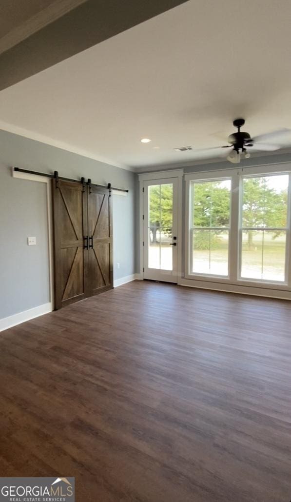 unfurnished room with a barn door, ceiling fan, and dark wood-type flooring