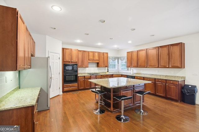 kitchen featuring sink, light stone counters, a kitchen island, black appliances, and hardwood / wood-style flooring