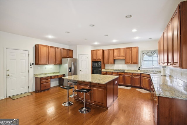 kitchen featuring black appliances, sink, tasteful backsplash, a kitchen island, and wood-type flooring