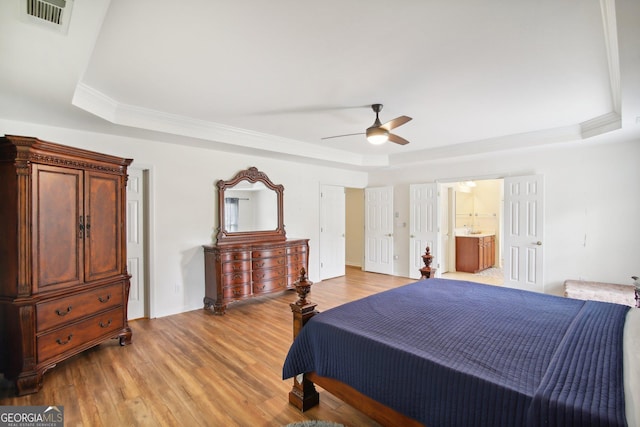 bedroom with ensuite bathroom, a raised ceiling, ceiling fan, and light hardwood / wood-style floors