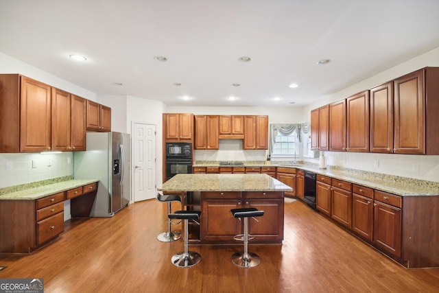 kitchen with black appliances, a kitchen island, a kitchen bar, and wood-type flooring