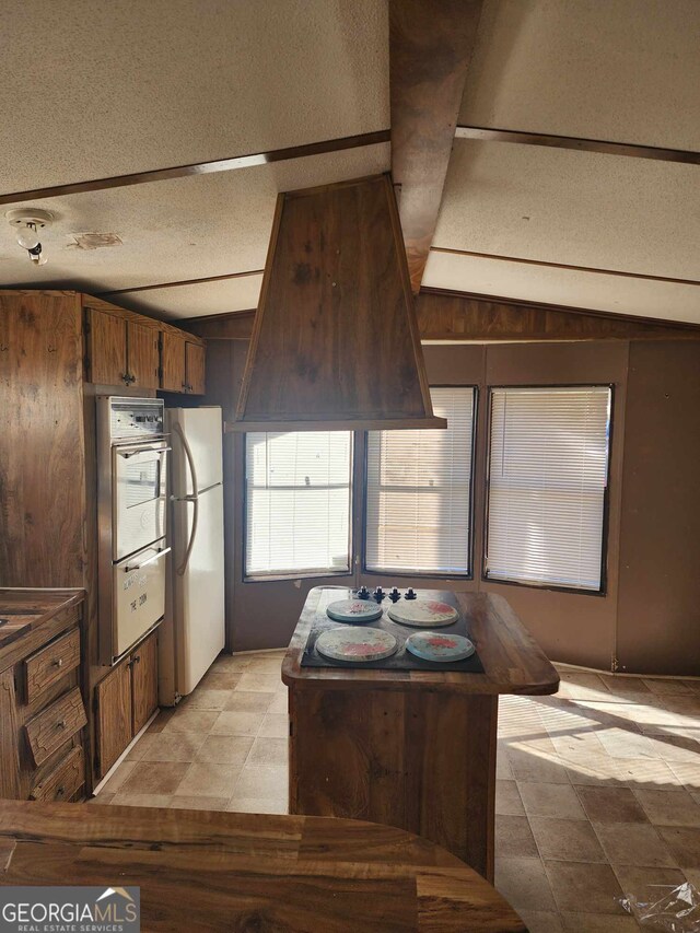 kitchen with a textured ceiling, white refrigerator, and vaulted ceiling