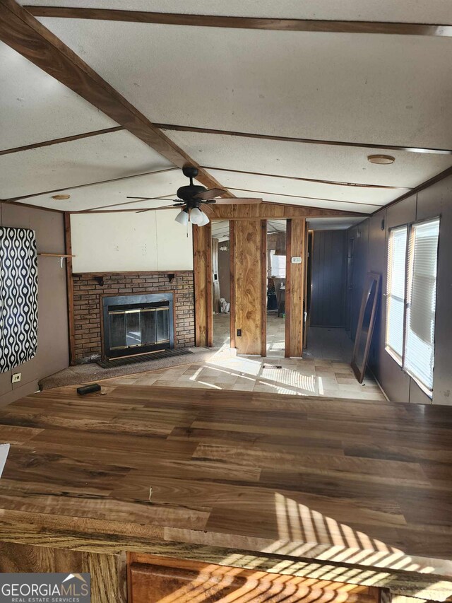 unfurnished living room featuring beamed ceiling, ceiling fan, and a fireplace