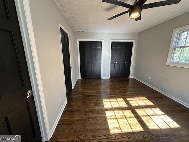 unfurnished bedroom with a textured ceiling, dark hardwood / wood-style flooring, ceiling fan, and multiple closets