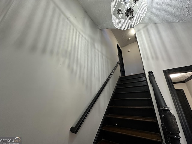 stairs with a textured ceiling and a notable chandelier