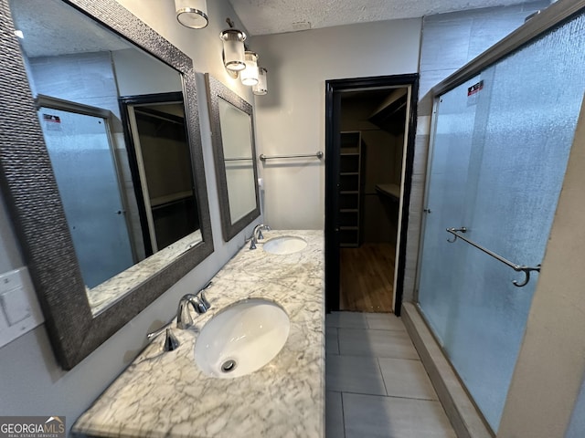 bathroom with tile patterned flooring, vanity, a shower with door, and a textured ceiling