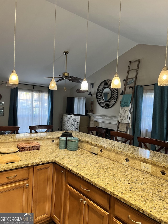 kitchen with ceiling fan, a kitchen breakfast bar, lofted ceiling, hanging light fixtures, and light stone counters