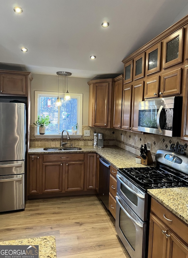 kitchen featuring light hardwood / wood-style flooring, stainless steel appliances, decorative light fixtures, light stone counters, and sink