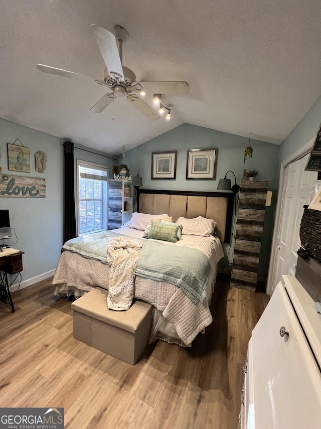 bedroom with ceiling fan, a closet, a textured ceiling, vaulted ceiling, and light hardwood / wood-style flooring