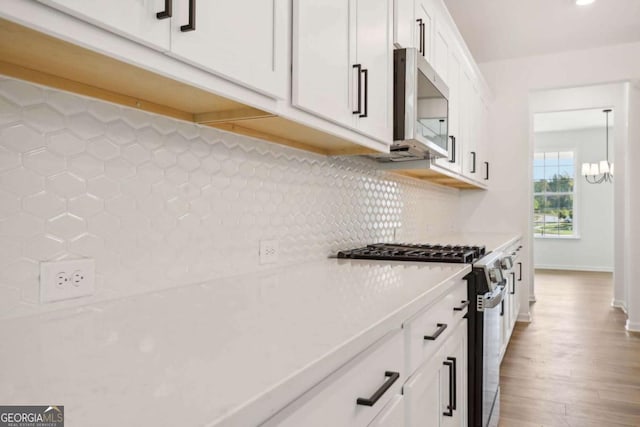 kitchen with hardwood / wood-style floors, a chandelier, decorative backsplash, white cabinets, and appliances with stainless steel finishes