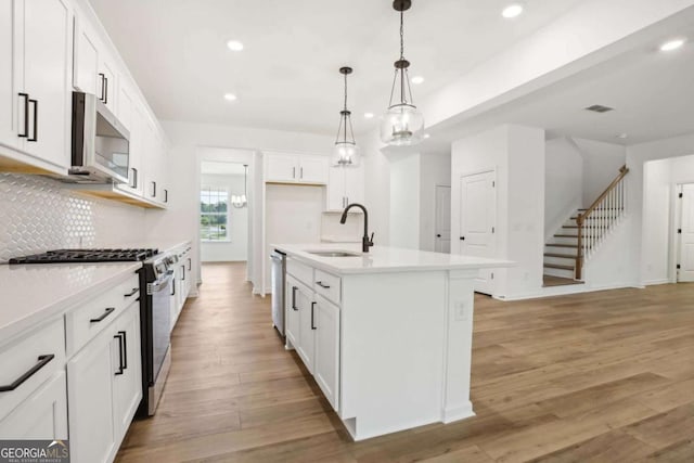 kitchen with stainless steel appliances, sink, pendant lighting, white cabinetry, and an island with sink