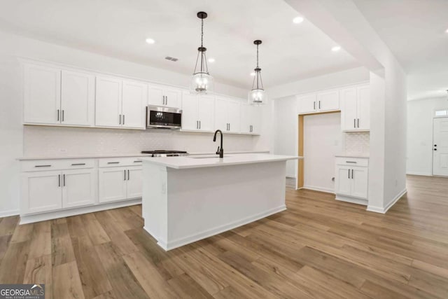 kitchen featuring a kitchen island with sink, white cabinets, light hardwood / wood-style floors, and decorative light fixtures