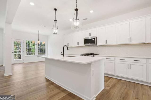 kitchen with a kitchen island with sink, sink, pendant lighting, white cabinets, and range