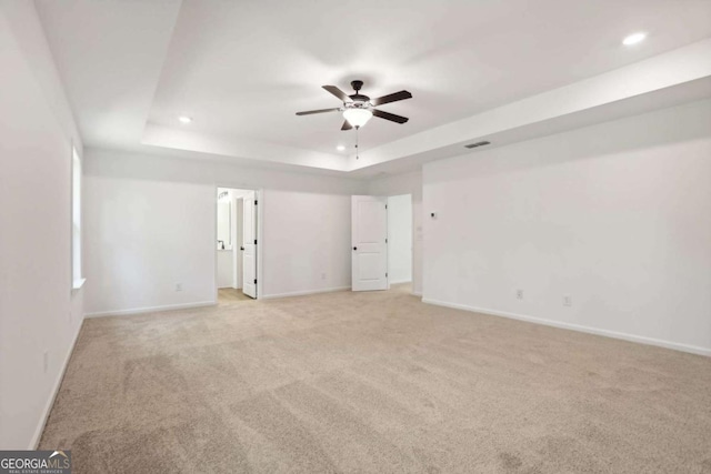 empty room featuring light carpet, a tray ceiling, and ceiling fan