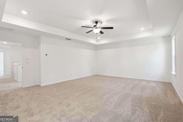 spare room featuring a tray ceiling, light carpet, and ceiling fan