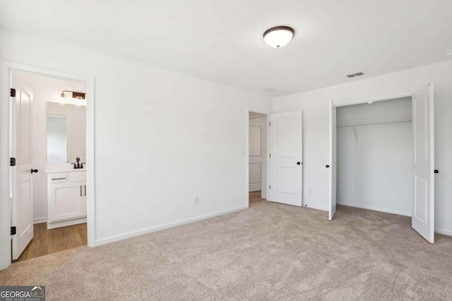 unfurnished bedroom with light carpet, ensuite bathroom, and a closet