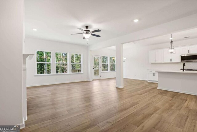 unfurnished living room featuring light hardwood / wood-style flooring, ceiling fan, a healthy amount of sunlight, and sink