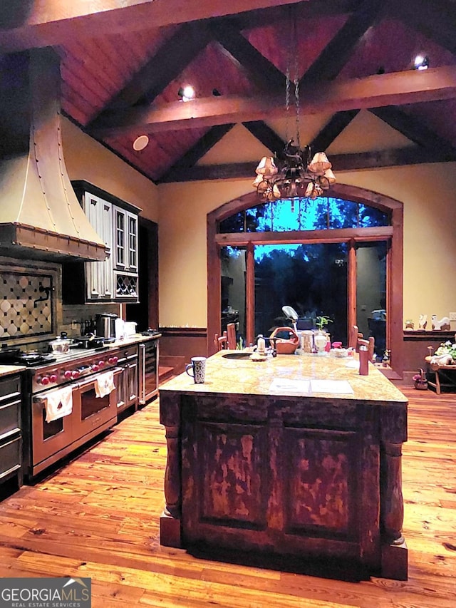 kitchen featuring lofted ceiling with beams, range with two ovens, extractor fan, beverage cooler, and a chandelier