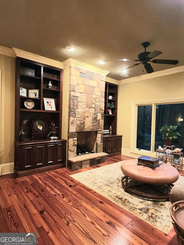 living room with ceiling fan, built in features, dark hardwood / wood-style floors, crown molding, and a fireplace