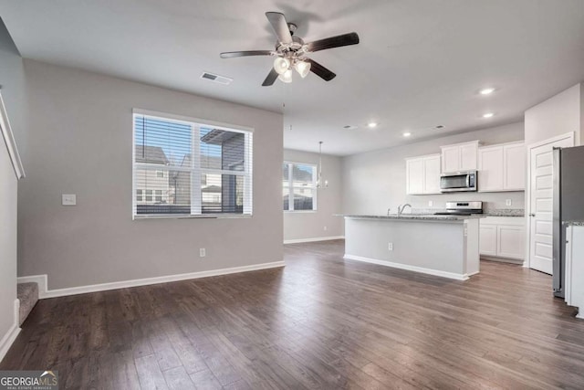 kitchen featuring dark wood-type flooring, a center island with sink, ceiling fan with notable chandelier, white cabinets, and appliances with stainless steel finishes