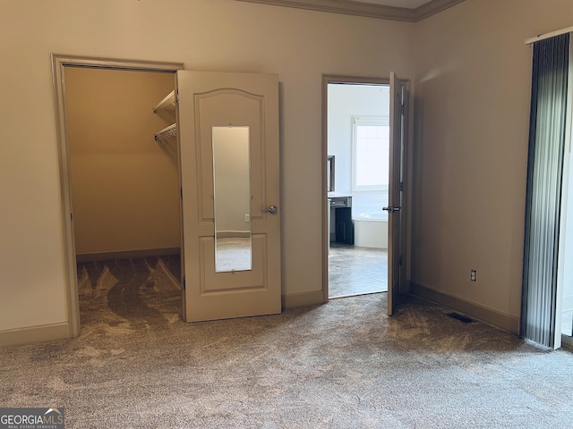 unfurnished bedroom with a walk in closet, crown molding, ensuite bath, carpet flooring, and a closet