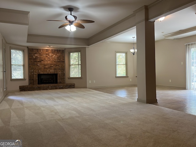 unfurnished living room featuring a fireplace, ceiling fan with notable chandelier, crown molding, and a healthy amount of sunlight