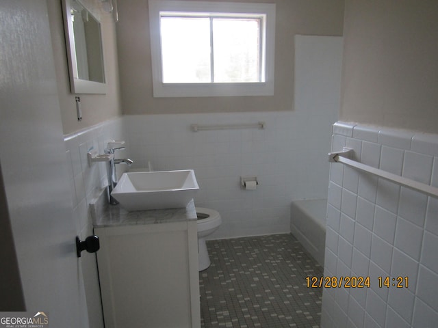 bathroom with toilet, vanity, tile patterned floors, and tile walls