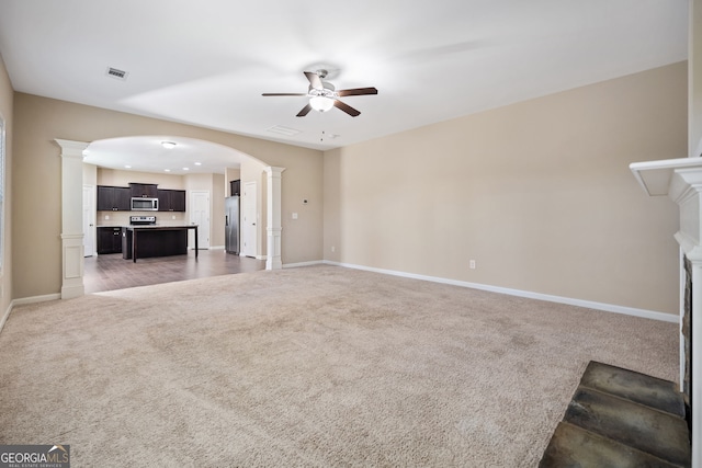 unfurnished living room featuring dark carpet, ceiling fan, and ornate columns