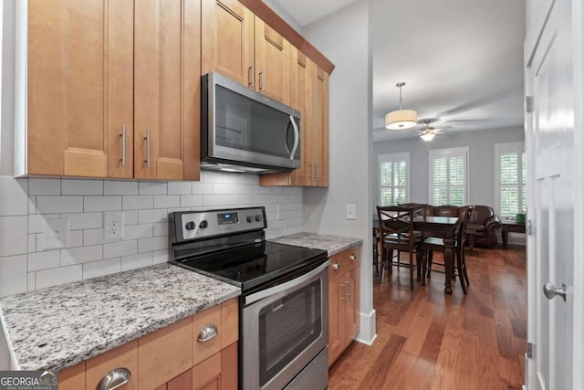 kitchen with light stone countertops, ceiling fan, dark wood-type flooring, decorative backsplash, and appliances with stainless steel finishes