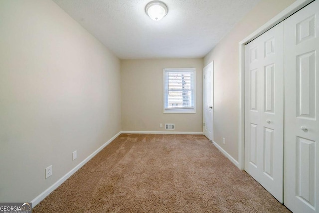 unfurnished bedroom with a textured ceiling, light carpet, and a closet